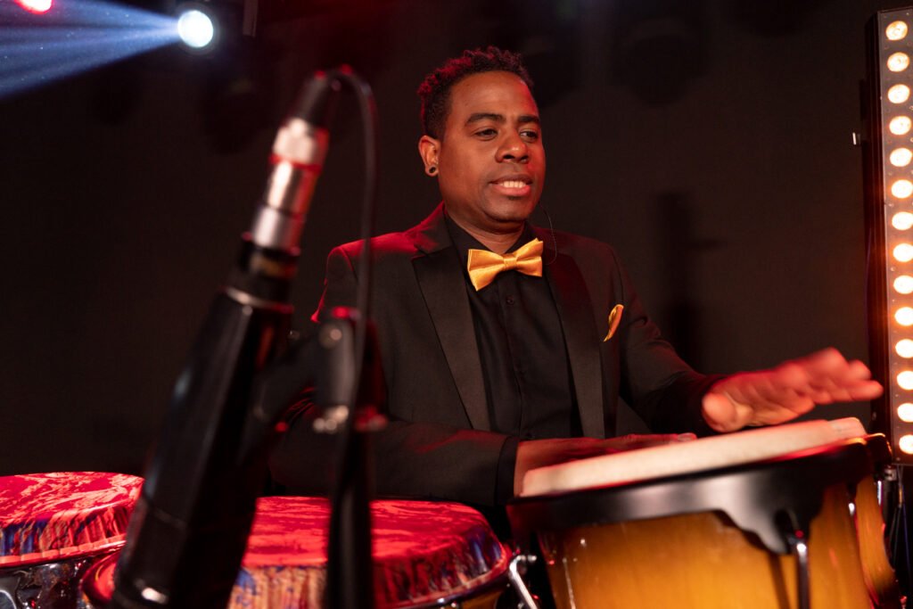 Bajo de escenario con músico tocando con instrumentos tradicionales en un evento cultural de AMAC, mostrando talento y pasión por la música latina.