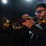 Juan tocando trompeta en un concierto con iluminación teatral para promover las actividades de AMAC en el ámbito artístico y musical.